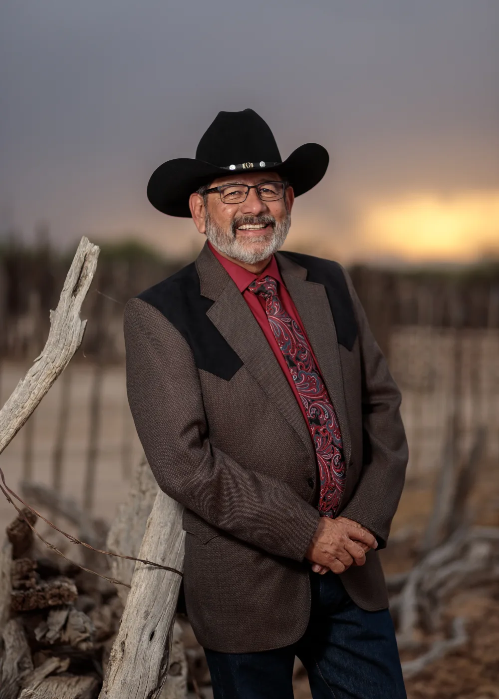 Portrait of a man in a black cowboy hat and western jacket leaning on a weathered fence post at sunset, by Casa de Baca Studios Portrait of a man in a black cowboy hat and western jacket leaning on a weathered fence post at sunset, by Casa de Baca Studios